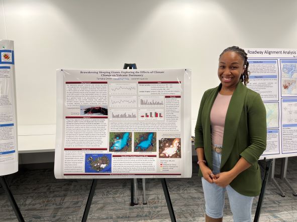 An MS student smiles in front of their poster