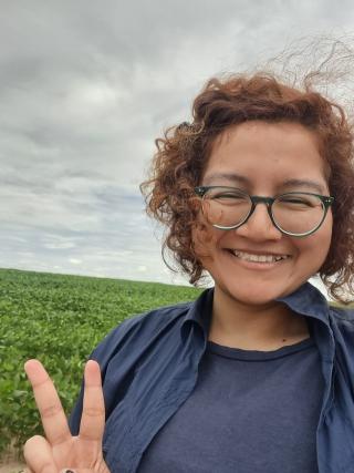 Woman with short curly brown hair and round-framed glasses 